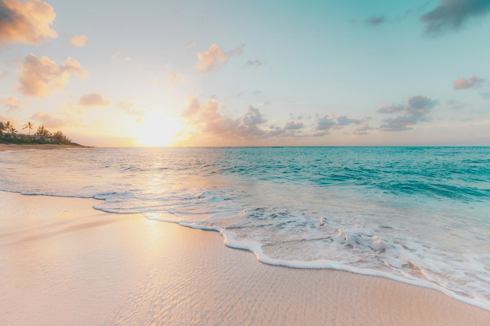 A sandy shoreline and small waves under a pale, sunlit sky.