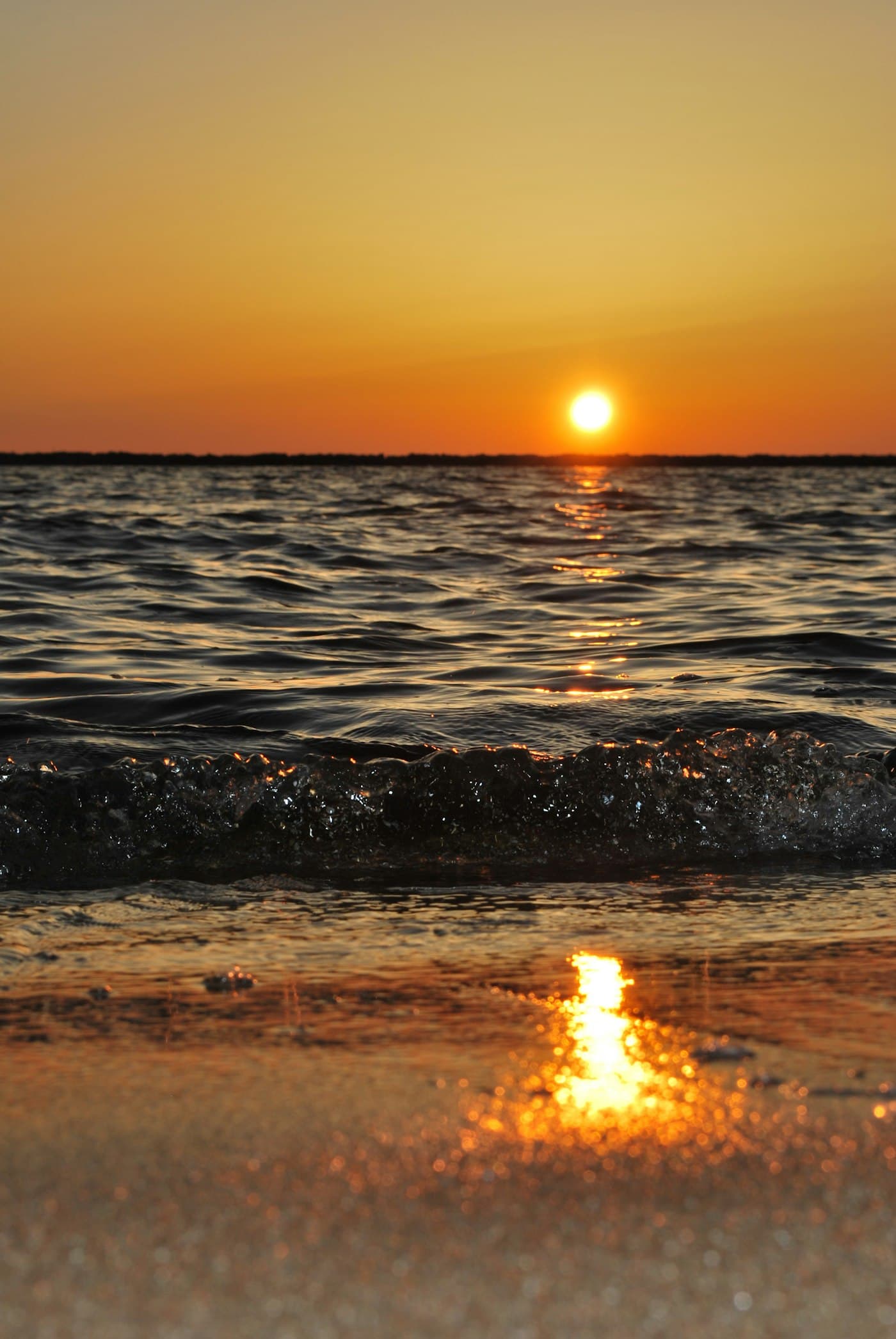 The sun low over the sea, with light reflecting on wet sand.